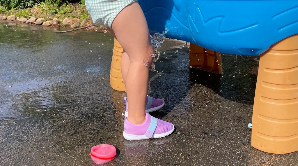 Toddler wearing purple water shoes at a splash table